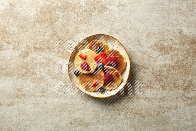 Five stacked mixed berries mini pancakes in an irregular plate on beige background