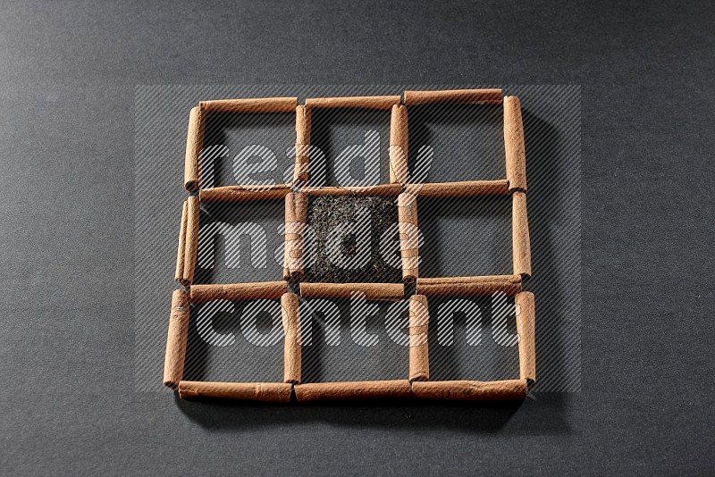 9 squares of cinnamon sticks full of tea in the middle surrounded by nutmeg, dried mint, cloves, dried basil, dried ginger, cinnamon, star anise and cardamom on black flooring