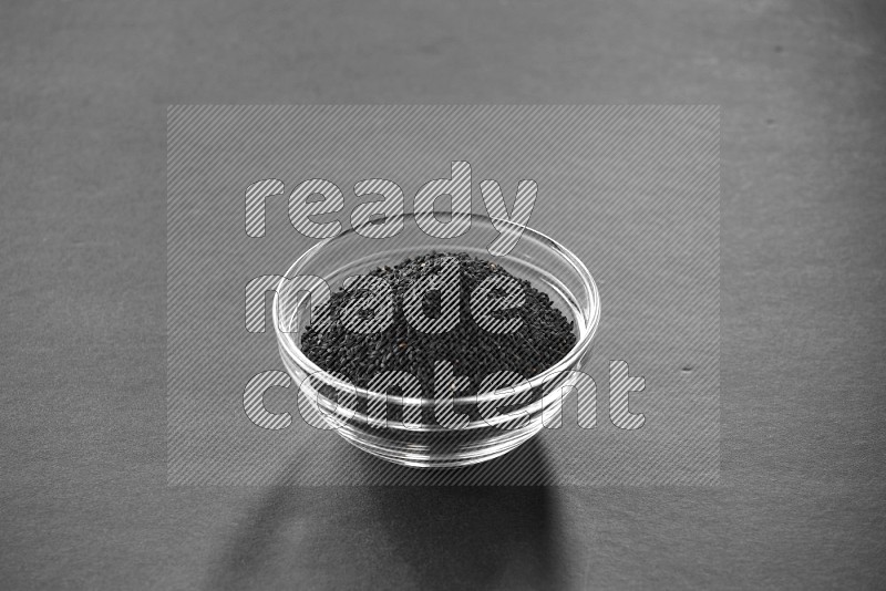 A glass bowl full of black seeds on black flooring