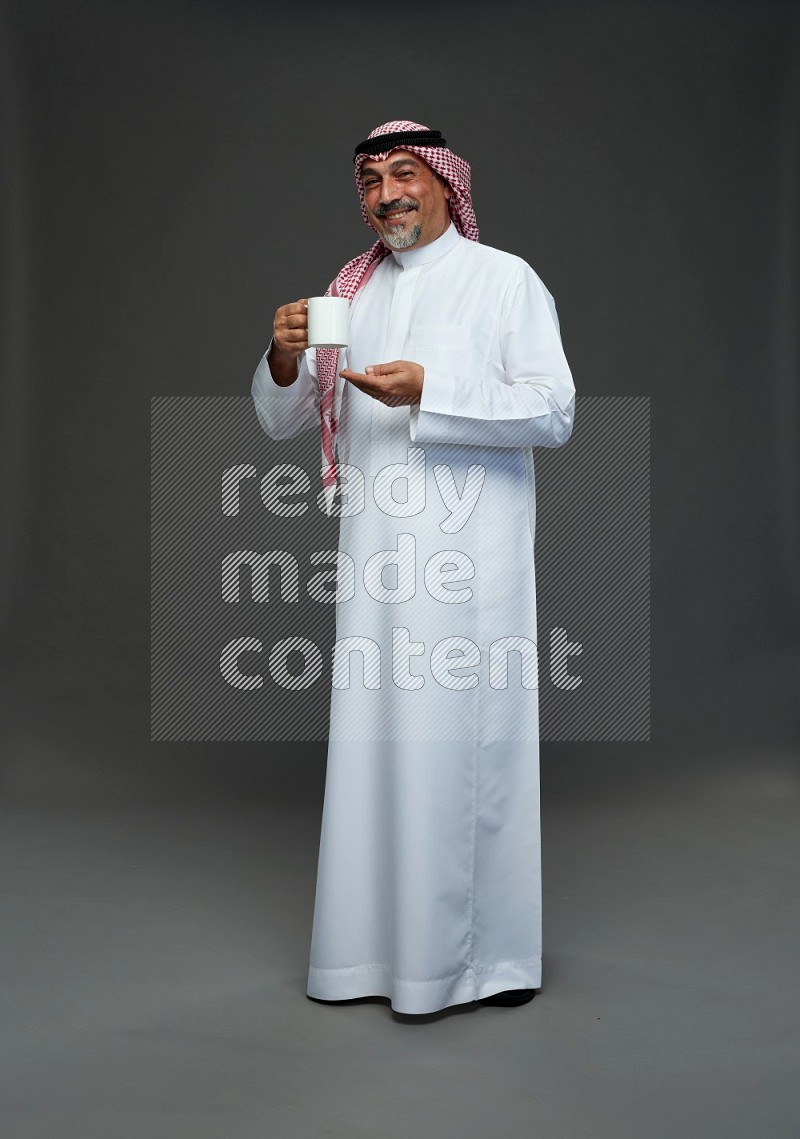 Saudi man with shomag Standing holding mug on gray background