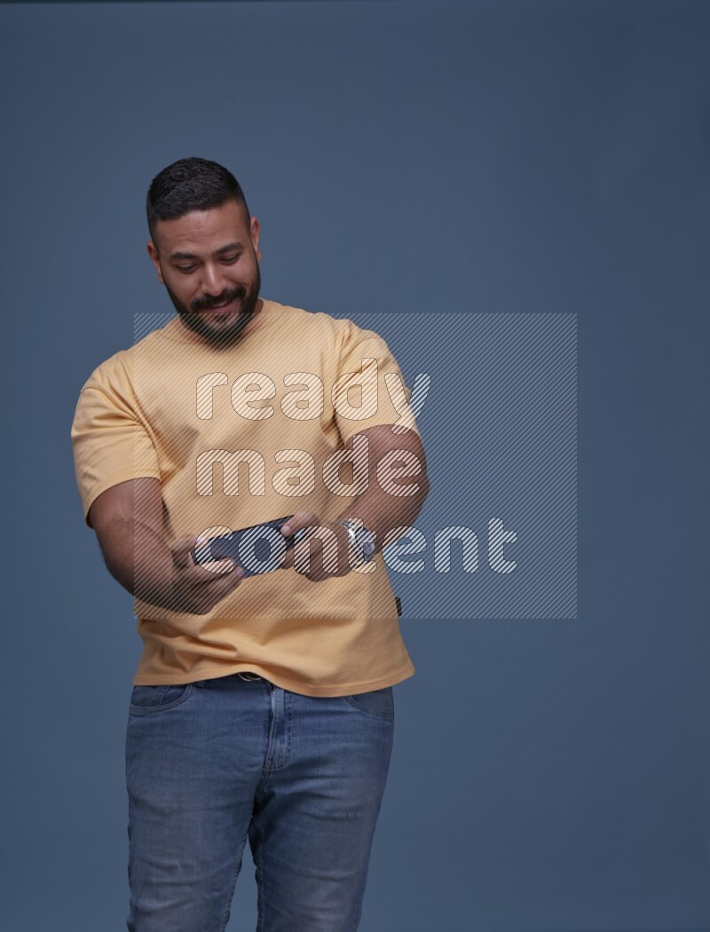 رجل يرتدي بنطال ازرق جينز وقميص اصفر بأكمام قصيره يلعب في جواله