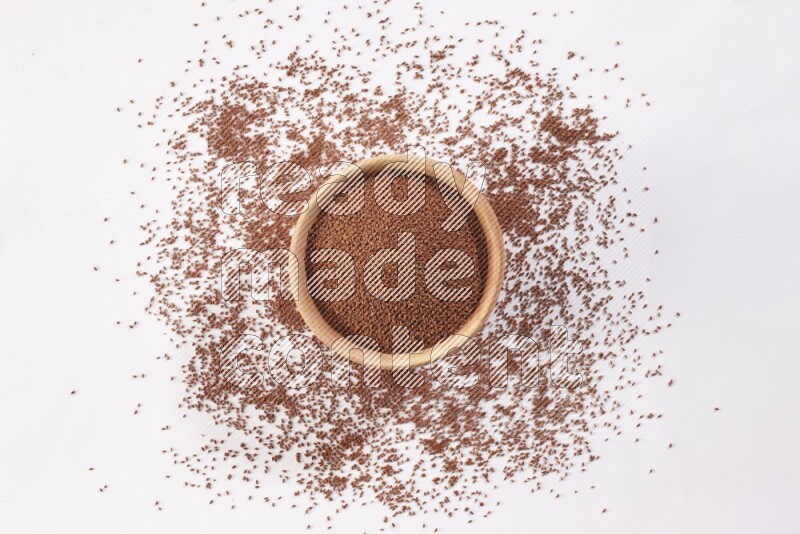 وعاء خشبي ممتلئ ببذور حب الرشاد مع المزيد من البذور متناثرة علي خلفية بيضاء