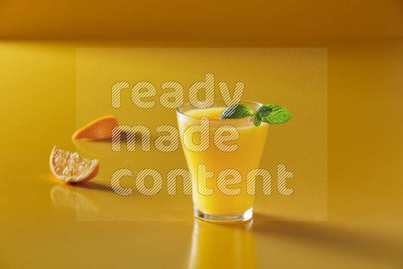 glass of orange juice with  mint on yellow background