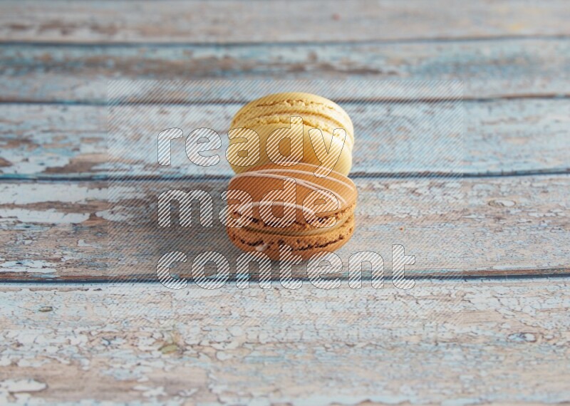 45º Shot of of two assorted Brown Irish Cream, and Yellow Vanilla macarons on light blue background