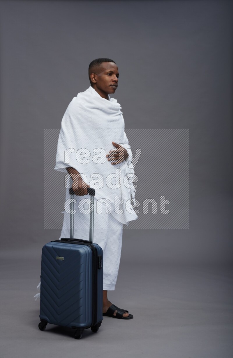 A man wearing Ehram Standing holding traveling bag on gray background