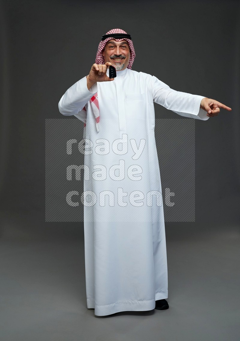 Saudi man with shomag Standing holding car key on gray background