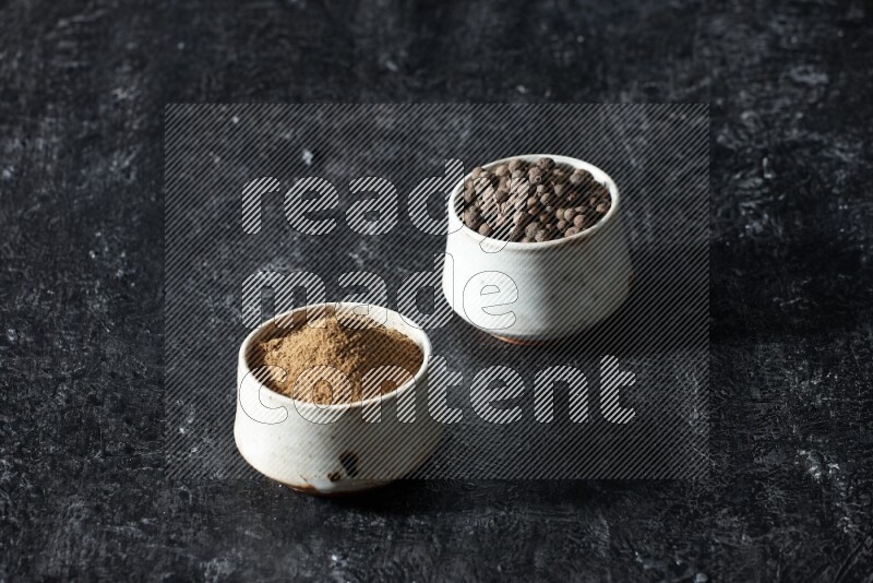2 beige bowls, one full of allspice powder and the other full of whole balls on a textured black flooring