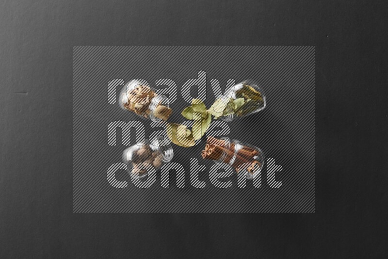 أوراق الغار وزنجبيل مجفف وقرفة وجوزة الطيب في أوعية زجاجية علي خلفية سوداء