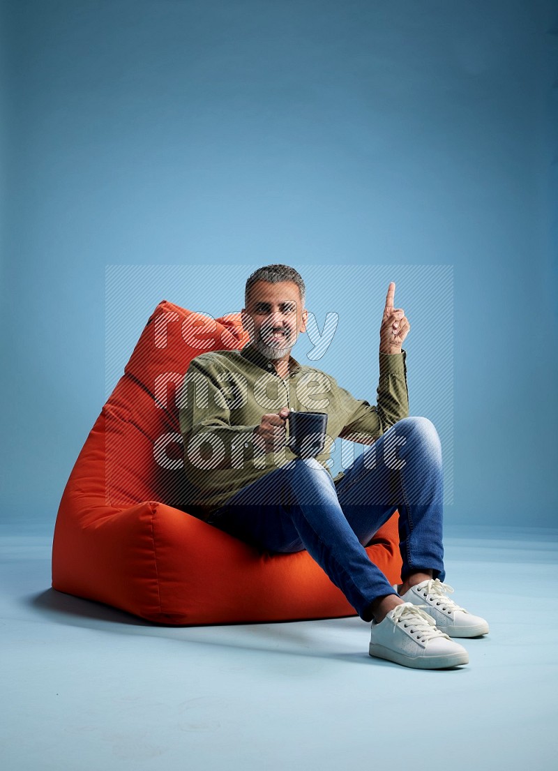 A man sitting on an orange beanbag and drinking coffee