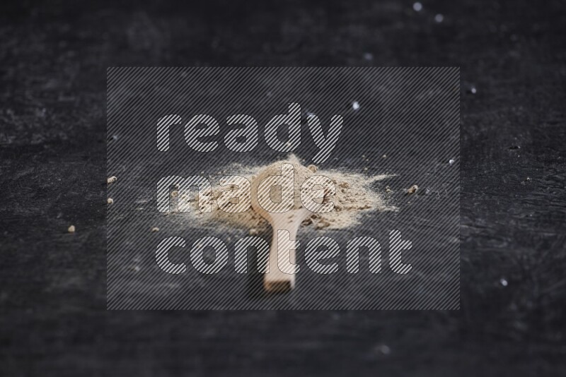 A wooden spoon full of garlic powder with scattered powder around it on a textured black flooring