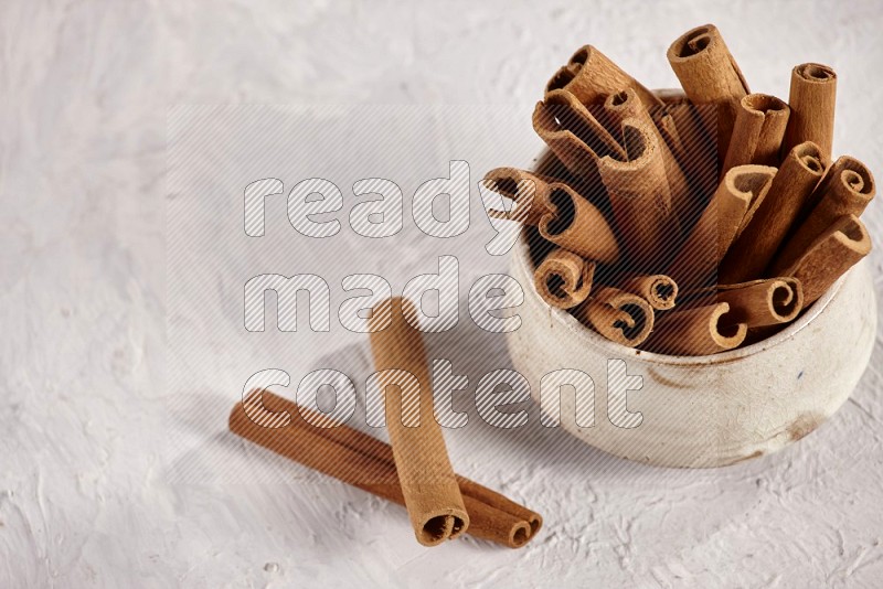 Cinnamon sticks in a beige bowl and more sticks beside it on white background