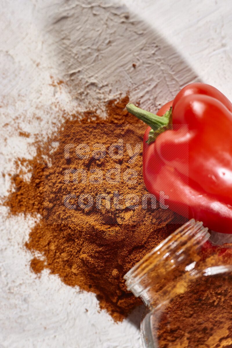 A glass jar full of ground paprika powder flipped with some spilling powder on white background