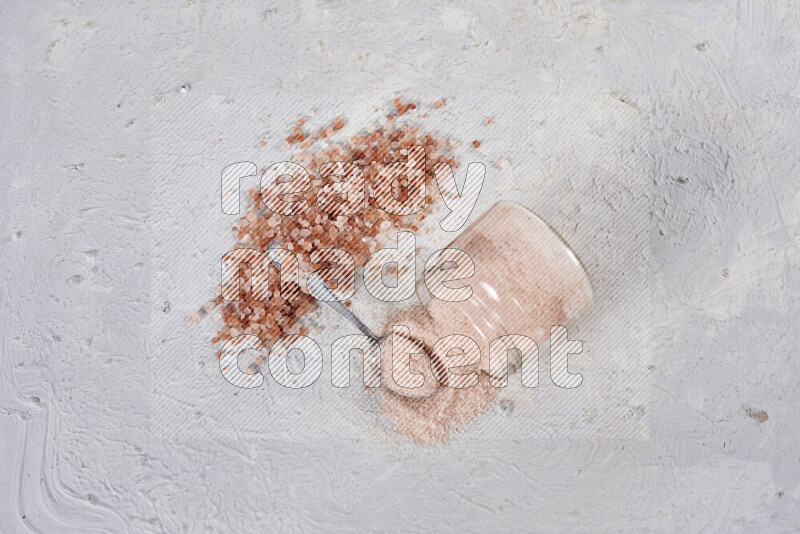 A glass jar full of fine himalayan salt with some himalayan crystals beside it on a white background