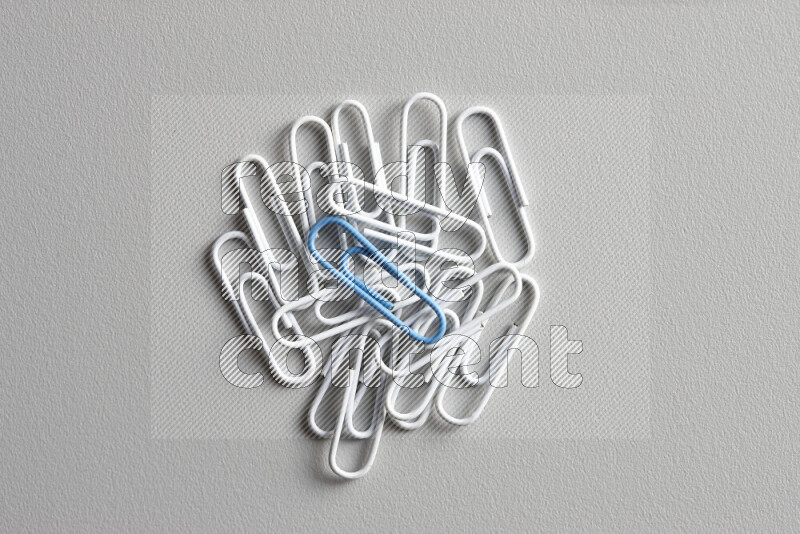 A blue paperclip surrounded by bunch of white paperclips on grey background