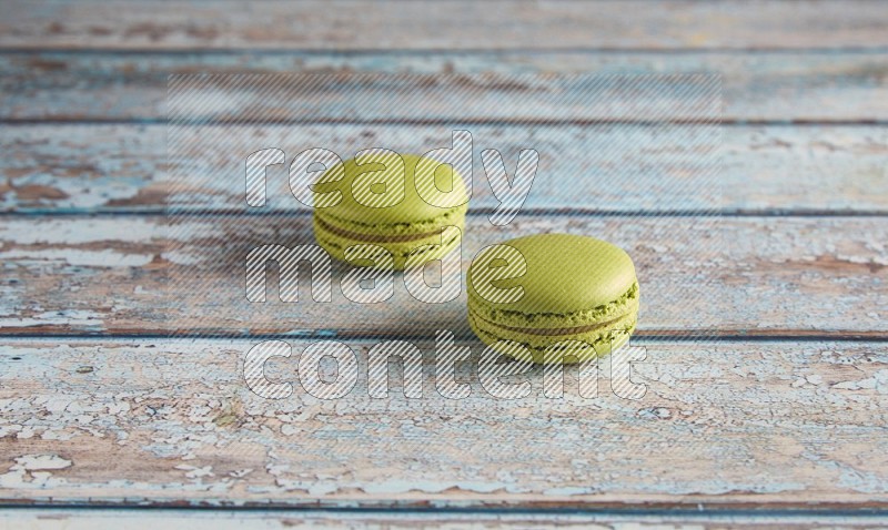 45º Shot of two Green Pistachio macarons on light blue wooden background