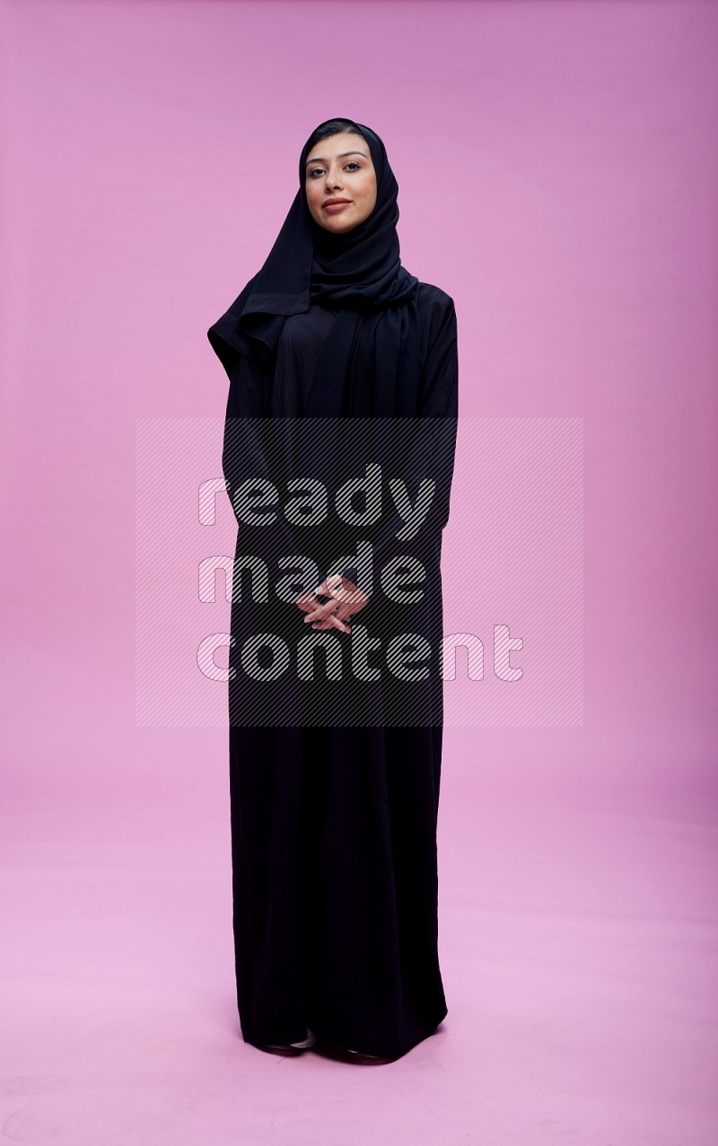Saudi woman wearing Abaya standing interacting with the camera on pink background