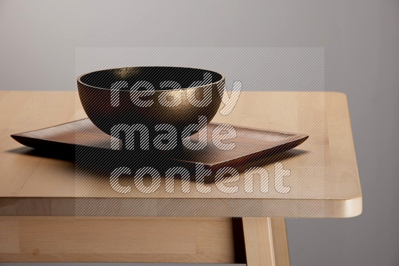 brass bowl placed on a rectangular wooden tray on the edge of wooden table