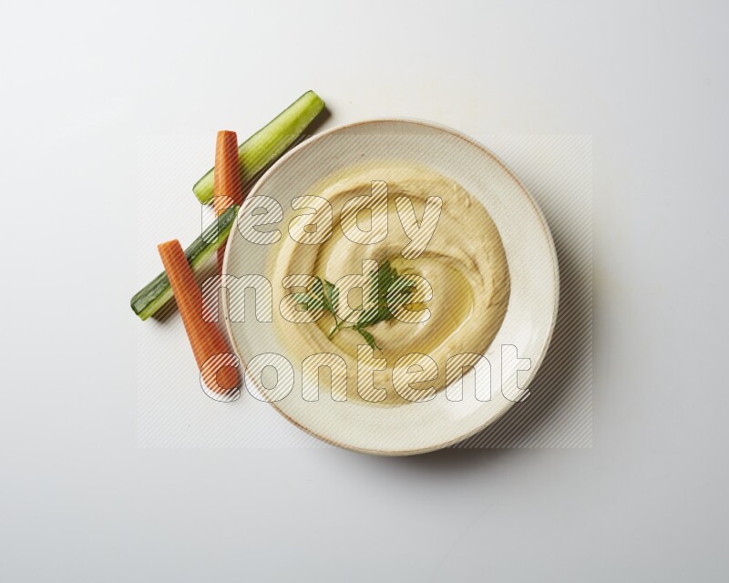 Hummus in a pottry plate garnished with parsley on a white back ground