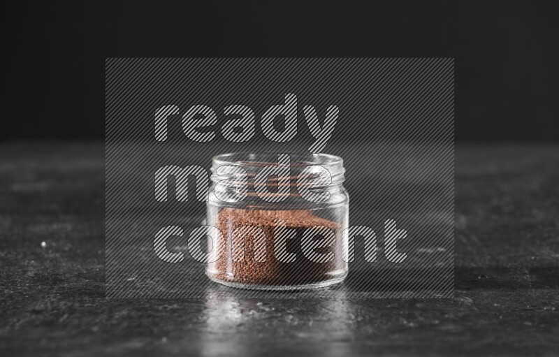 A glass jar full of garden cress seeds on a textured black flooring