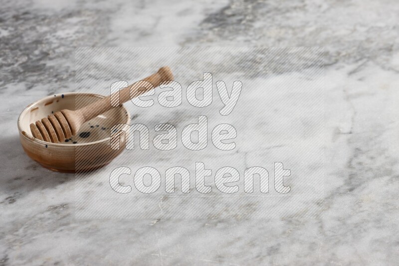 وعاء فخاري متعدد الألوان مع ملعقة عسل خشبية بداخله على خلفية من الرخام الرمادي