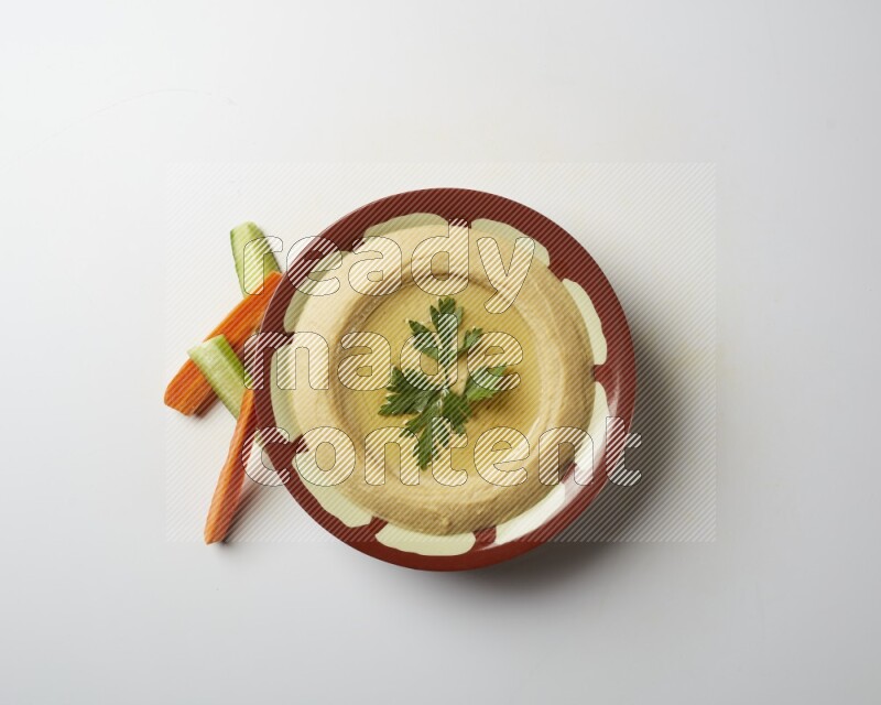 Hummus in a traditional plate garnished with parsley on a white background