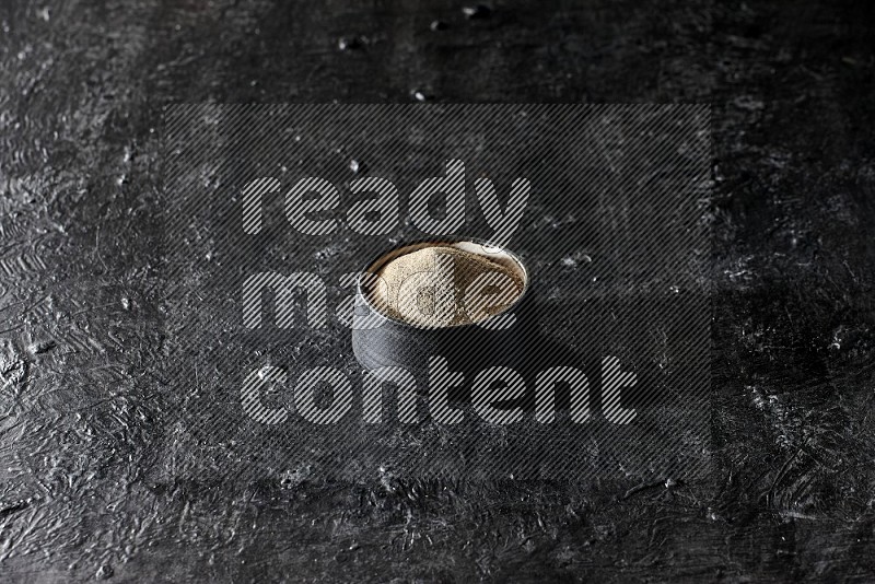 Black pottery bowl full of white pepper powder on textured black flooring