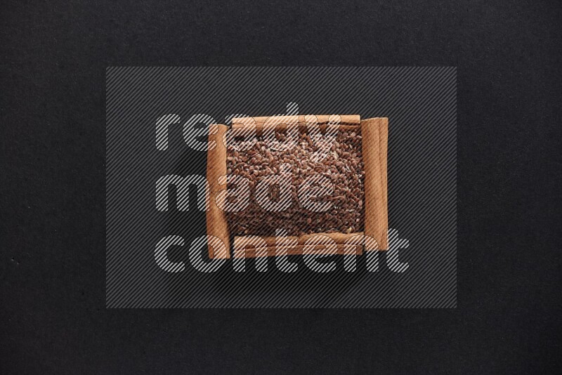 A single square of cinnamon sticks full of flaxseeds on black flooring