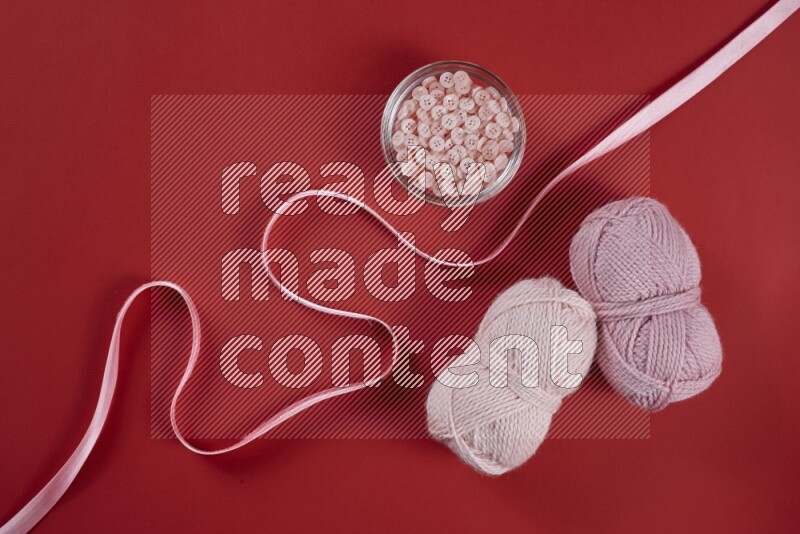 A pink and red collection of sewing and tailoring tools arranged on a red background