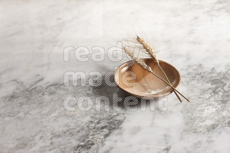 Wheat stalks on multicolored pottery plate on grey marble background