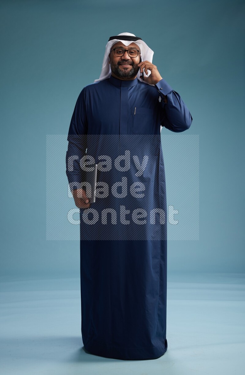Saudi Man with shimag Standing talking on phone on blue background