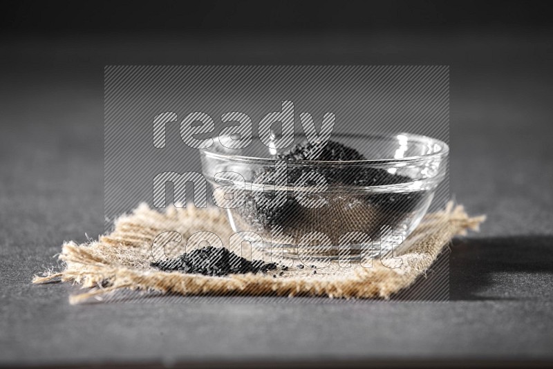 A glass bowl full of black seeds and seeds on burlap fabric on a black flooring in different angles