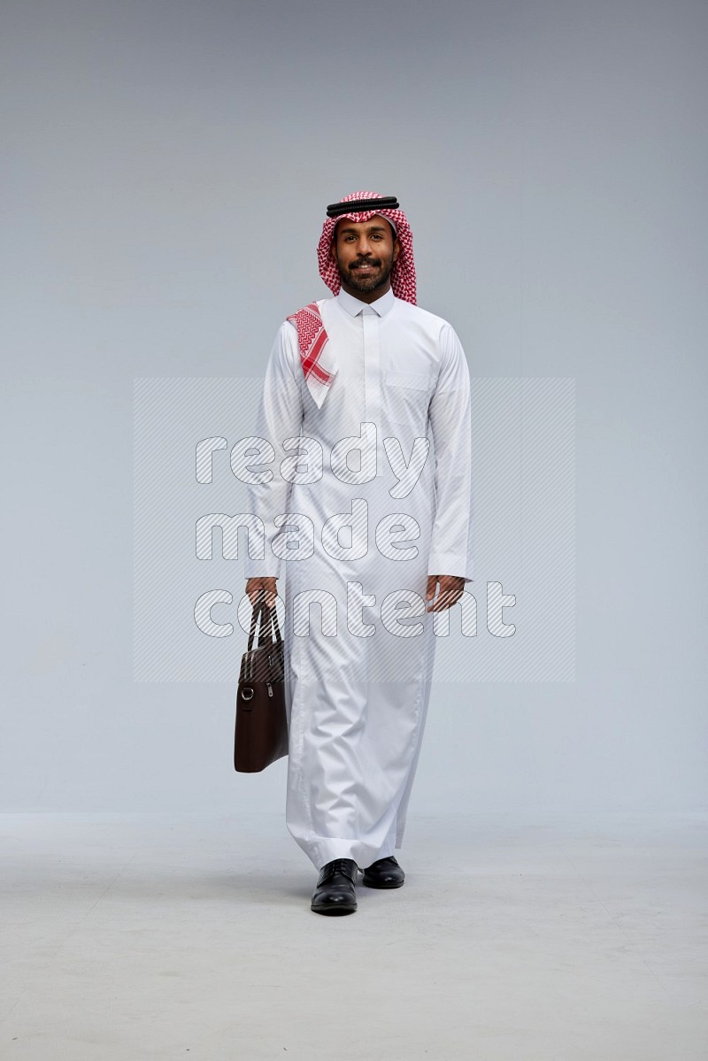 Saudi man Wearing Thob and shomag standing holding bag on Gray background