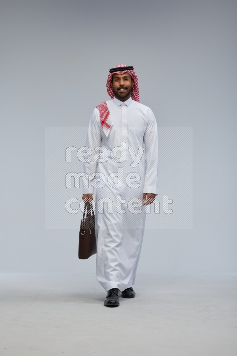 Saudi man Wearing Thob and shomag standing holding bag on Gray background