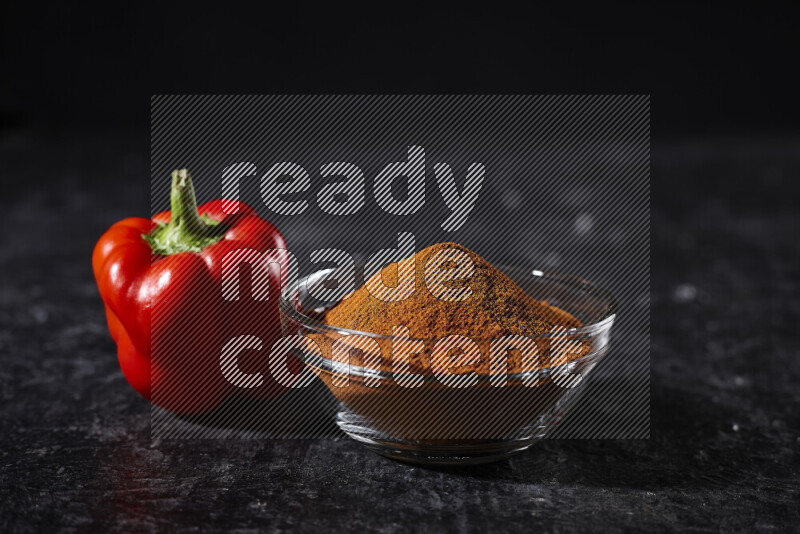 A glass bowl full of ground paprika powder on black background