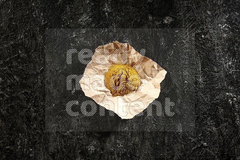 Turmeric powder in a crumpled piece of paper on textured black flooring