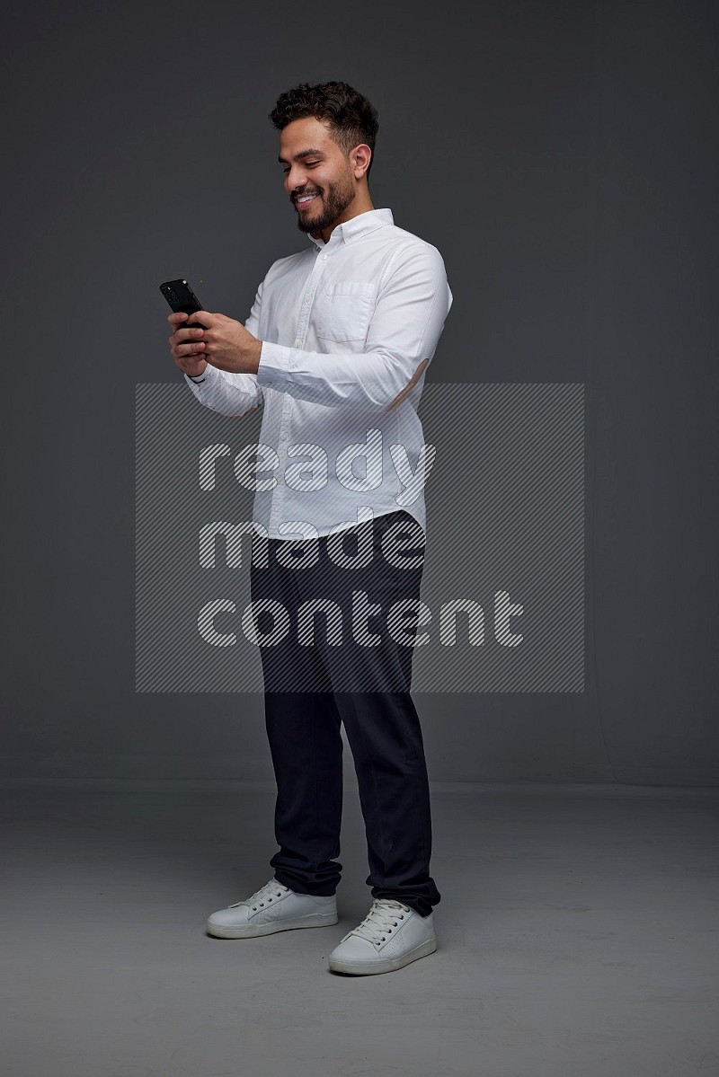 A man wearing smart casual standing and using his phone eye level on a gray background