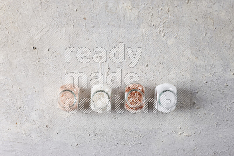 4 glass jars filled with table salt, coarse sea salt, fine himalayan salt and coarse himalayan salt on white background