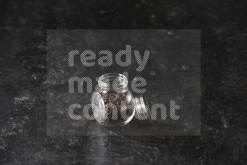 وعاء بهارات زجاجي ممتلئ بحبوب القرنفل على أرضية سوداء