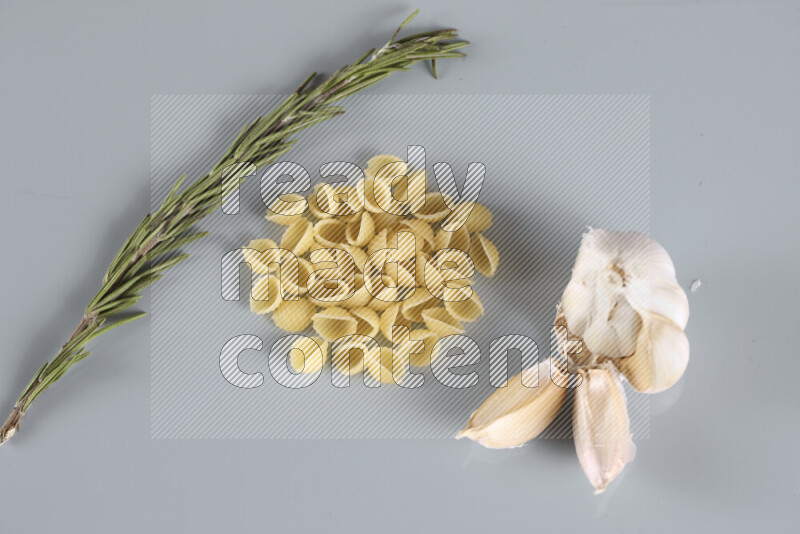 Raw pasta with different ingredients such as cherry tomatoes, garlic, onions, red chilis, black pepper, white pepper, bay laurel leaves, rosemary, cardamom and mushrooms on light blue background