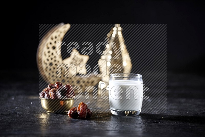 Dates in a metal bowl with milk beside golden lanterns in a dark setup