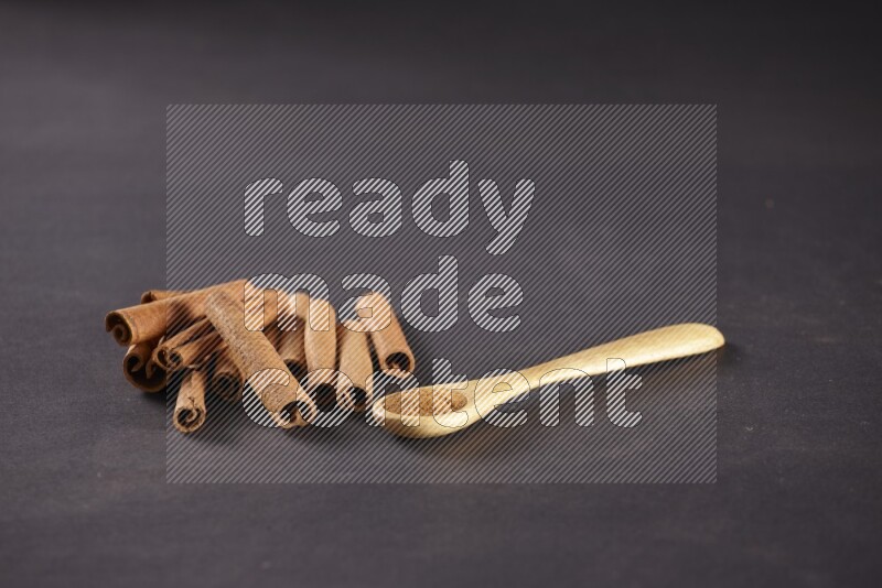 Cinnamon sticks stacked beside a wooden spoon full of cinnamon powder on black background
