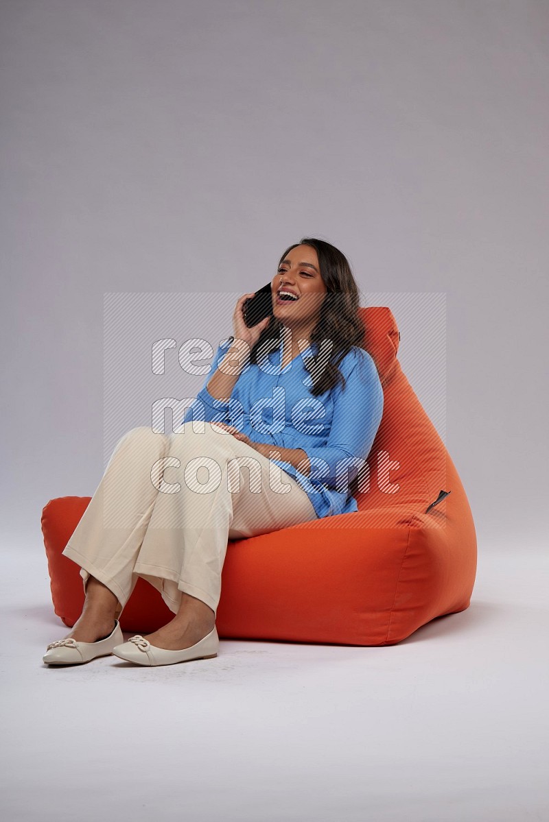 A woman sitting on an orange beanbag and talking on the phone