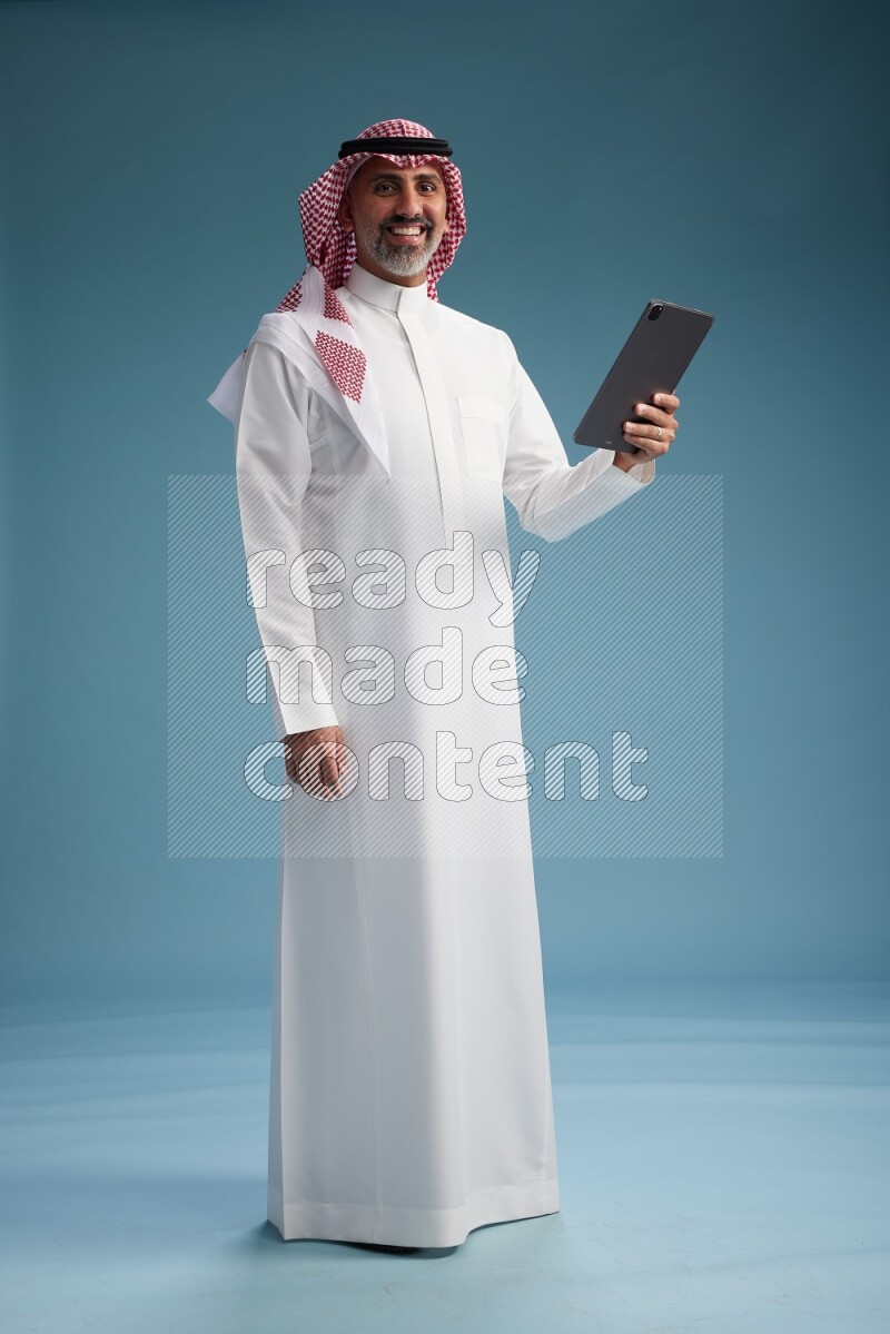Saudi man wearing thob and shomagh with tablet on Blue background