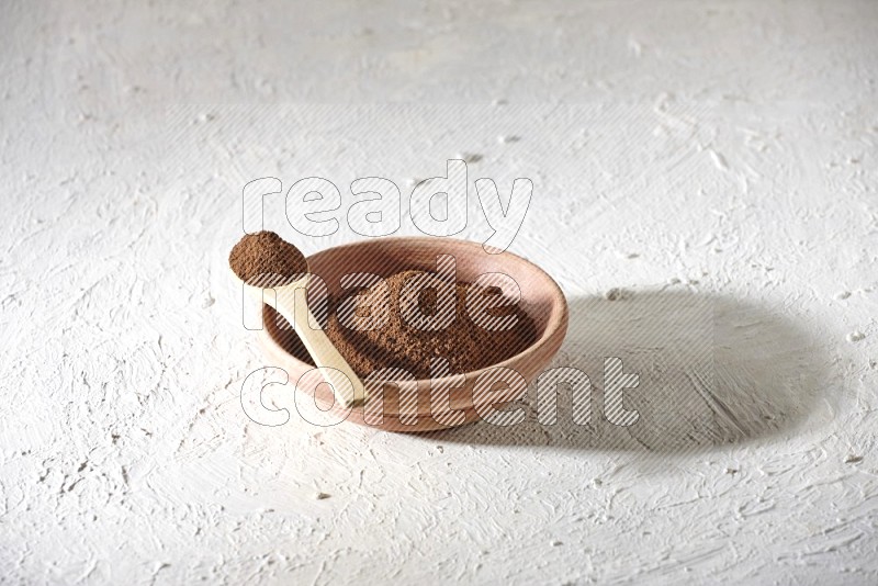 A wooden bowl and a wooden spoon full of cloves powder on a textured white flooring