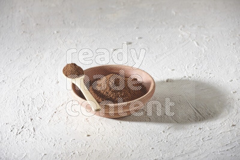 A wooden bowl and a wooden spoon full of cloves powder on a textured white flooring
