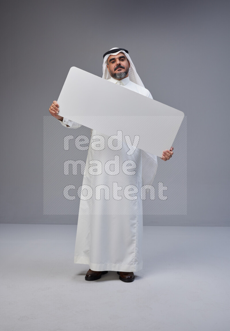 Saudi man Wearing Thob and white Shomag standing holding board on Gray background