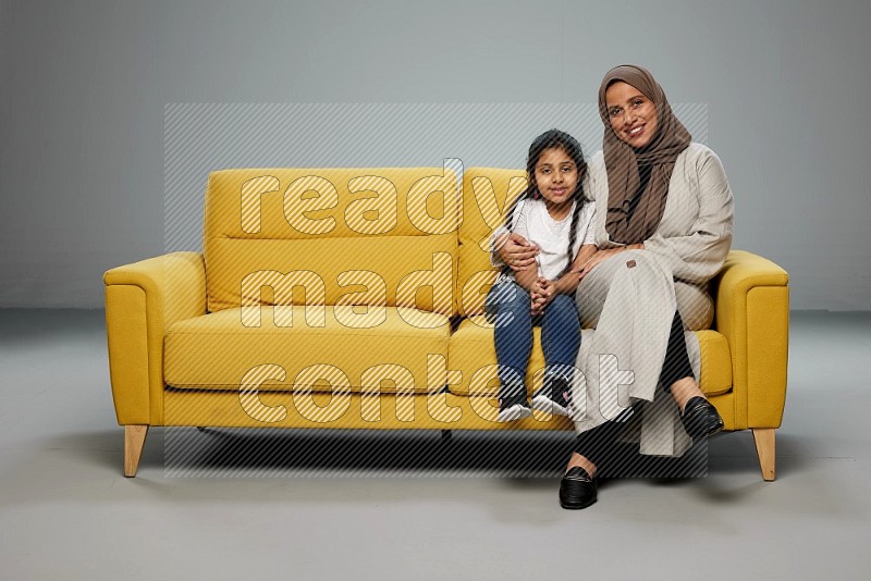 A girl with her mother sitting and interacting with the camera on gray background