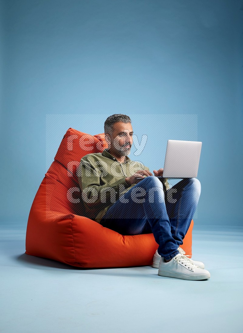 A man sitting on an orange beanbag and working on laptop