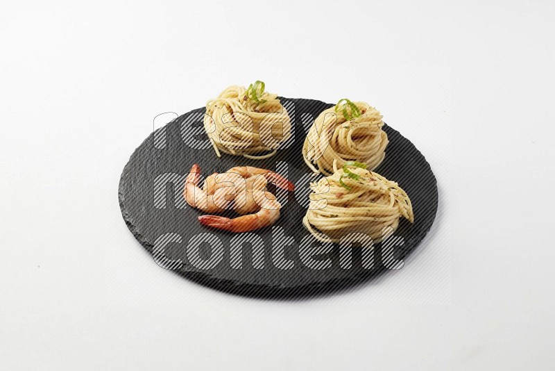 spaghetti nests with white sauce and shrimp on a black slate on a white background