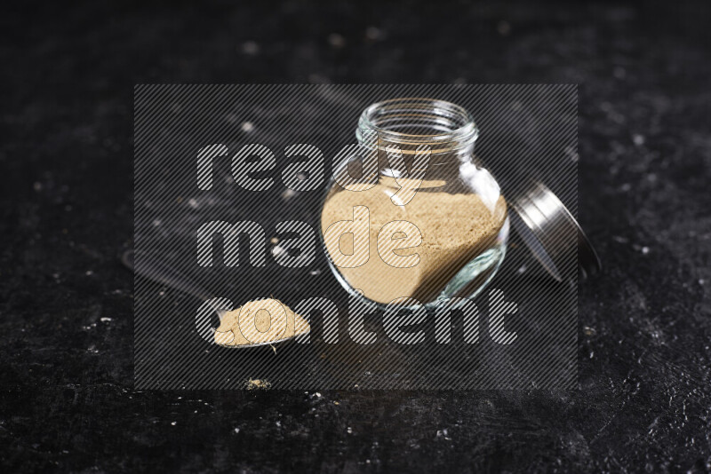 A glass jar full of ground ginger powder on black background